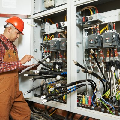 adult electrician builder engineer worker with electric scheme plan in front of fuse switch board
